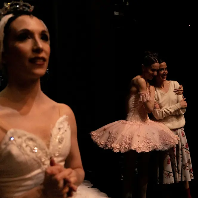 Ballet dancers embracing backstage after a performance while others wait in the wings.