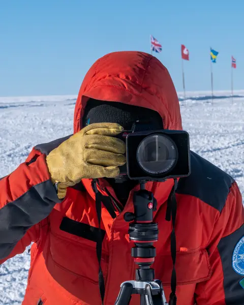 Person takes a photo in a snowy landscape with European flags in the background.