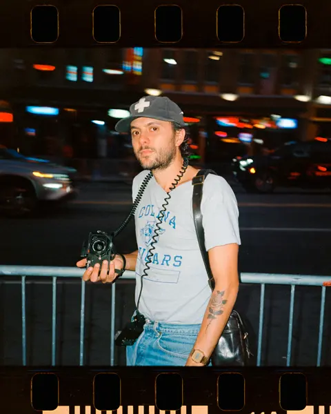 Joe Greer with a Leica M6 in his hand standing at a street at night.