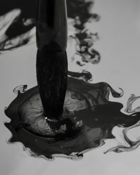 Brush dips into dark ink that spreads in the water.