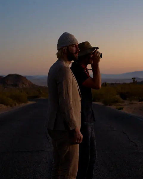 Garrett and Gantry Hill in a desert landscape at sunset, one looking through a camera.