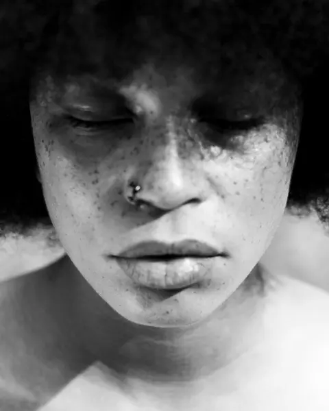 A close-up of a person with closed eyes and Afro hairstyle in black and white