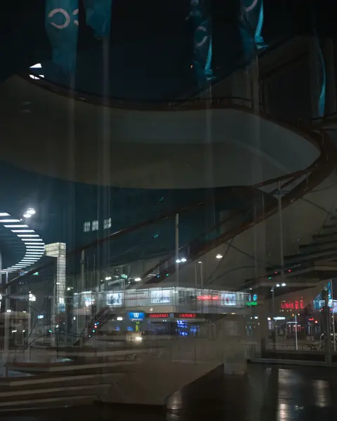Reflection of a spiral staircase and a city at night in the glass front of a building.