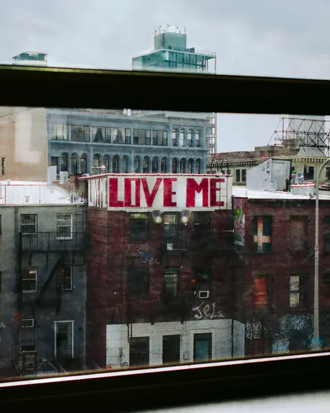 View from a window of a city with a building bearing the graffiti ‘LOVE ME’.