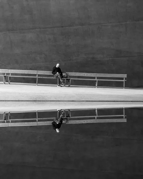 A man sits in front of a building by the water