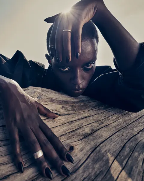 A young woman is peeking out from behind a tree trunk