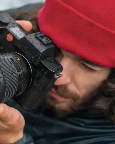 Close-up of a photographer with a red cap looking through the camera