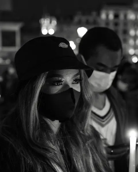 Close-up of a woman and man wearing masks and holding candles in a city at night.