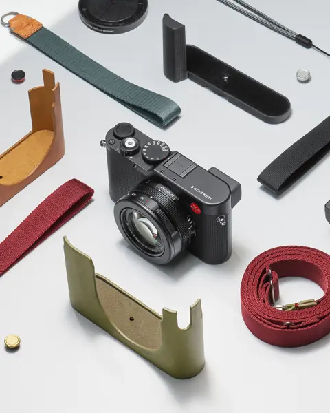Leica camera with various straps, protective covers and accessories on a light background.