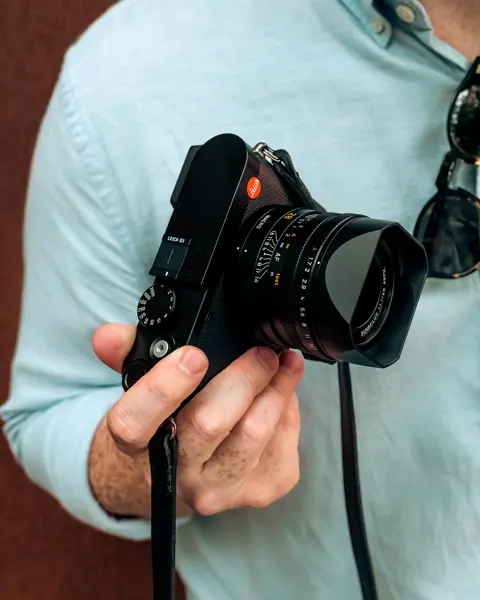 A man wearing a blue shirt holding a Leica camera in his right hand