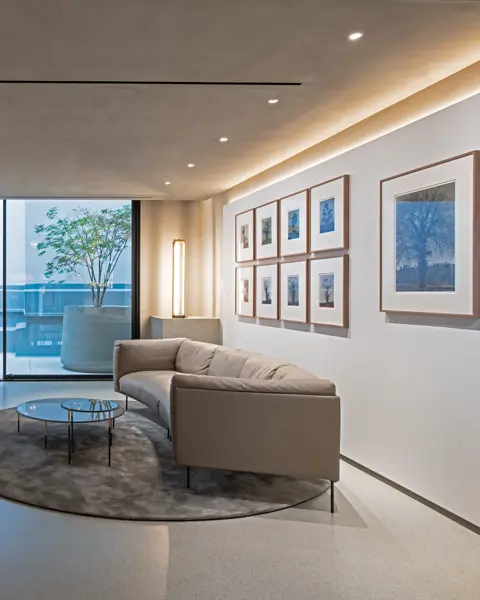 Modern room with sofa, glass table, photographs of trees and view of terrace with red seats.