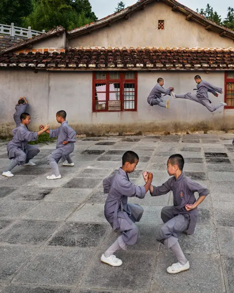 Shaolin monks practise martial arts in the courtyard in front of a traditional building