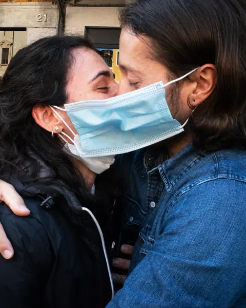 A couple wearing face masks hug and kiss in a street