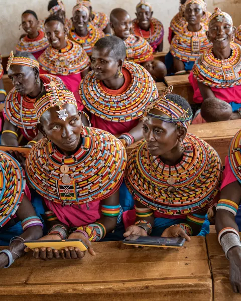 Women from the Samburu tribe in Kenya sitting on a wooden bench in traditional clothes and smiling.