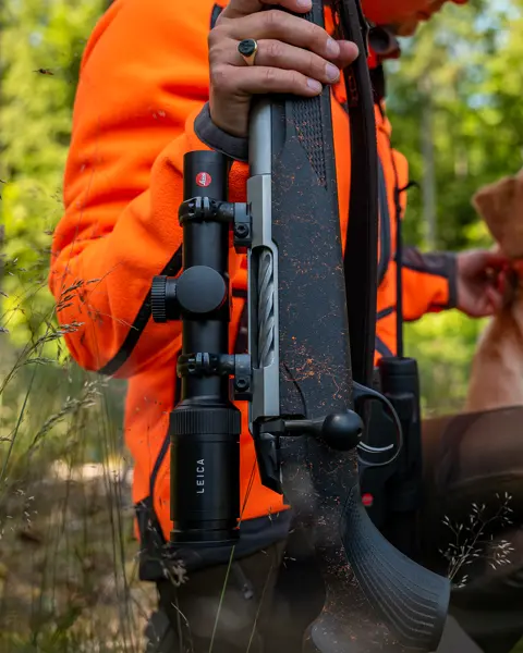 The Leica Amplus is the focus of the picture, while a huntress has knelt down and is holding her weapon.