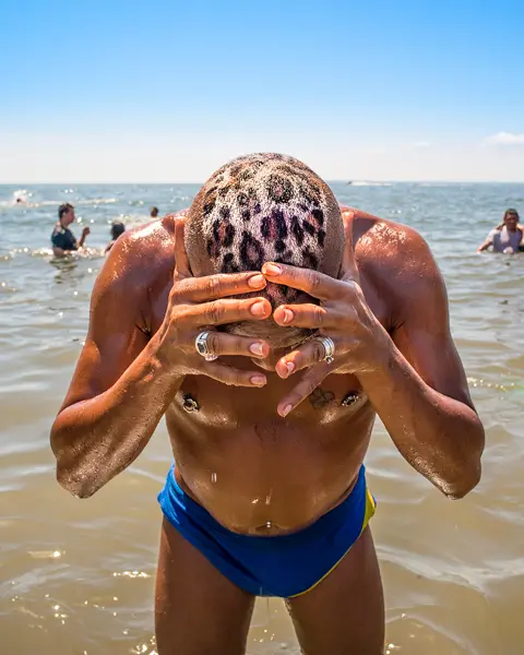 A man with a leopard print on his head is standing in the water. Several people are bathing in the sea around him.