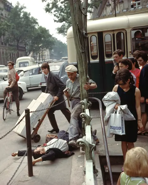 A young man in a suit and tie lies on his back with arms stretched above his head, directly next to the metro station