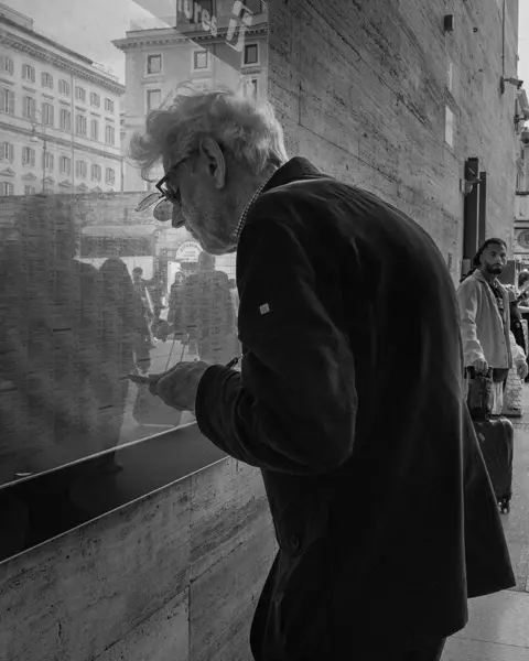 Elderly man in the city looking at a train timetable behind a pane of glass.
