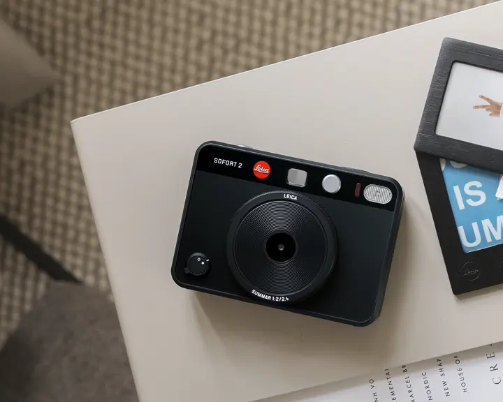 A Leica instant camera on a table with framed prints next to it.