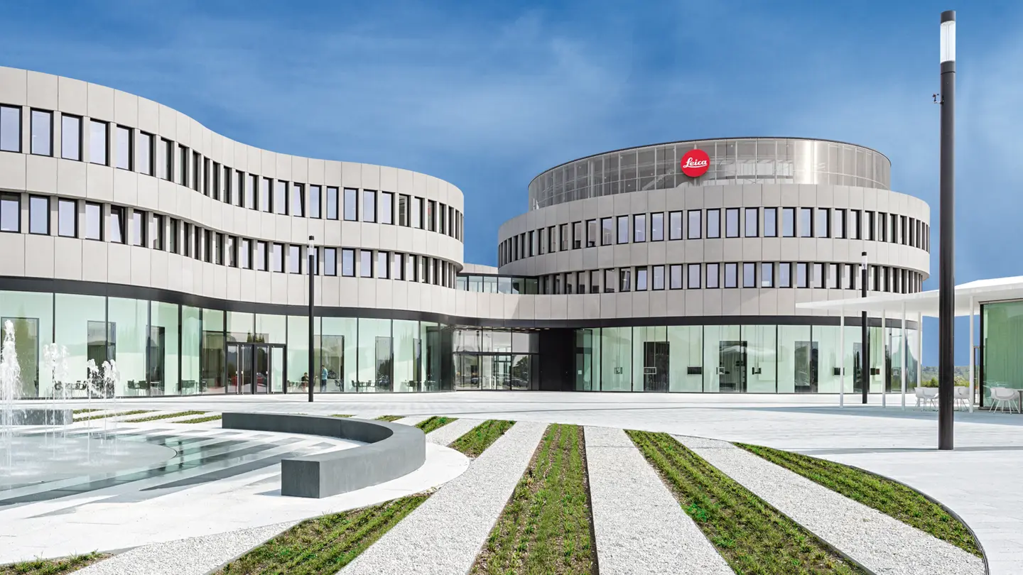 Modern architecture with Leica logo and curved glass facades and a fountain in front of the building.