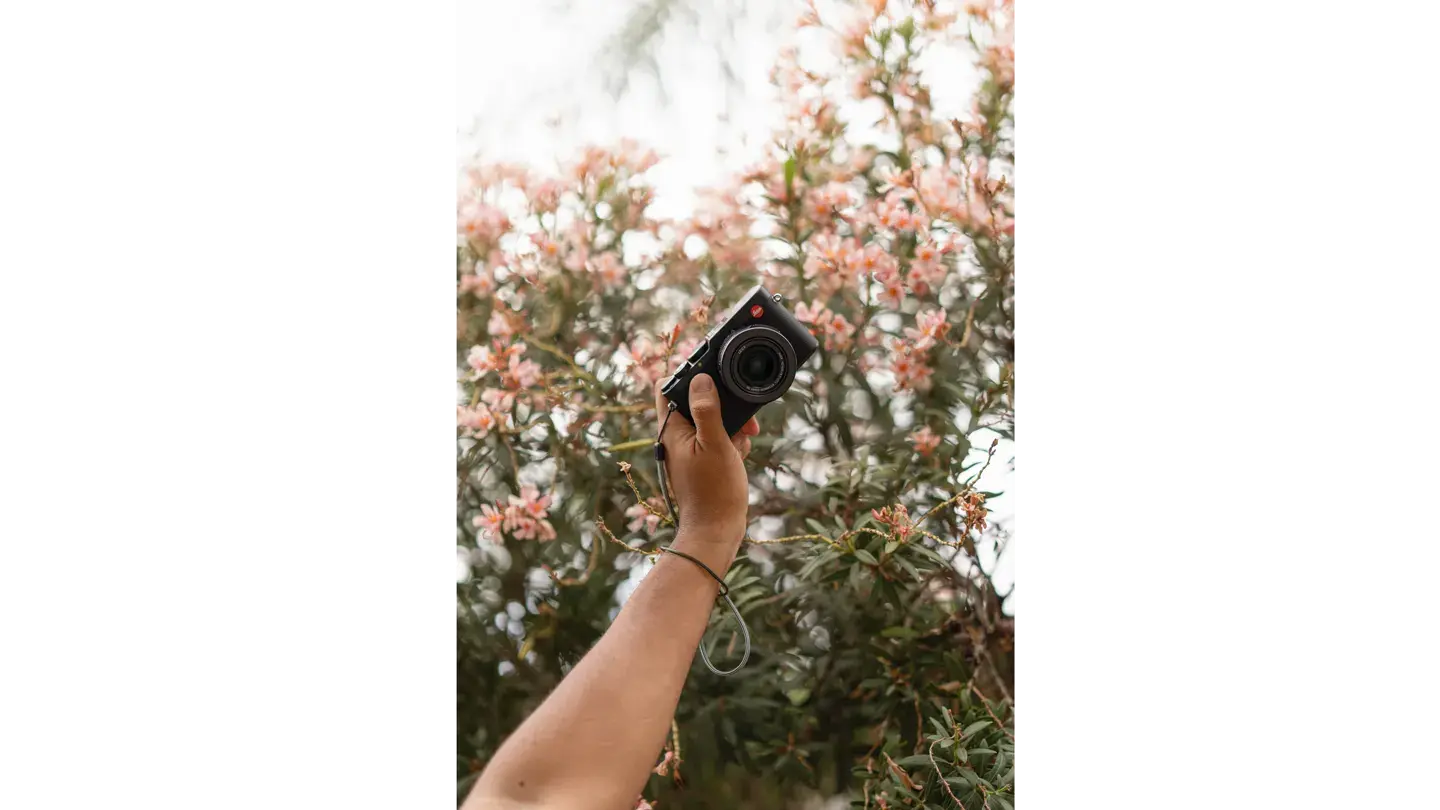 outstretched arm with a Leica Camera in his hand in front of a flower bush