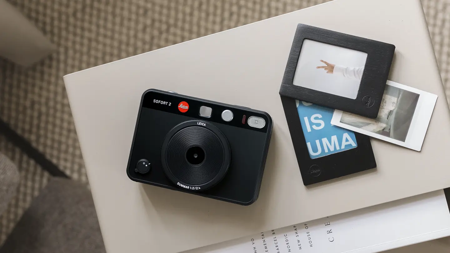 A Leica instant camera on a table with framed prints next to it.