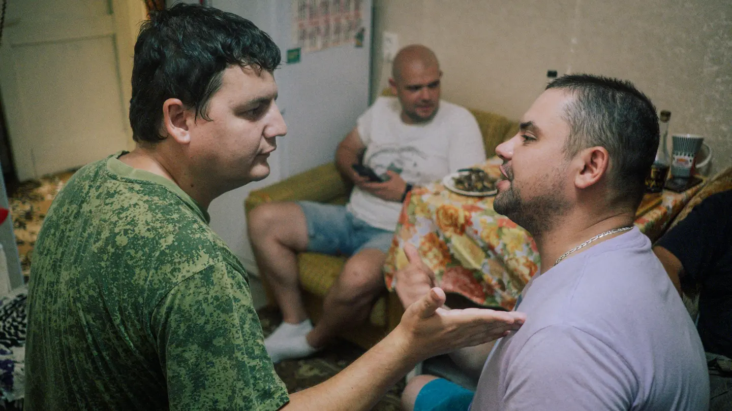 Three men are sitting on a table and two of them are discussing.