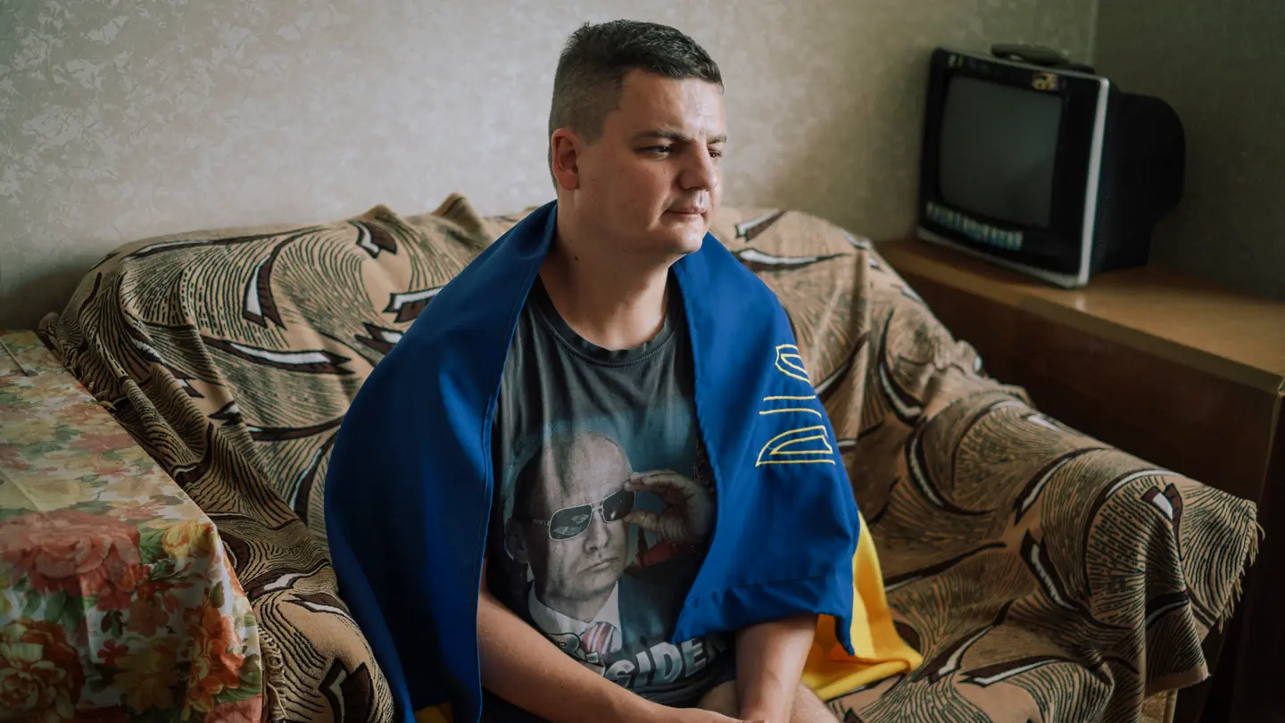 A man sitting on the couch with a Moldovan flag draped around his shoulders.