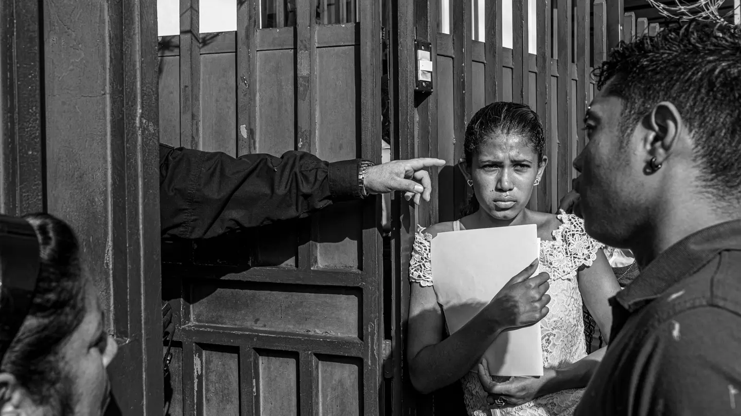 Two women and a man standing in front of a door from which someone is sticking their arm out.