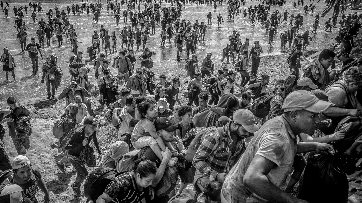 A stream of refugees runs through water and then up a mountain.