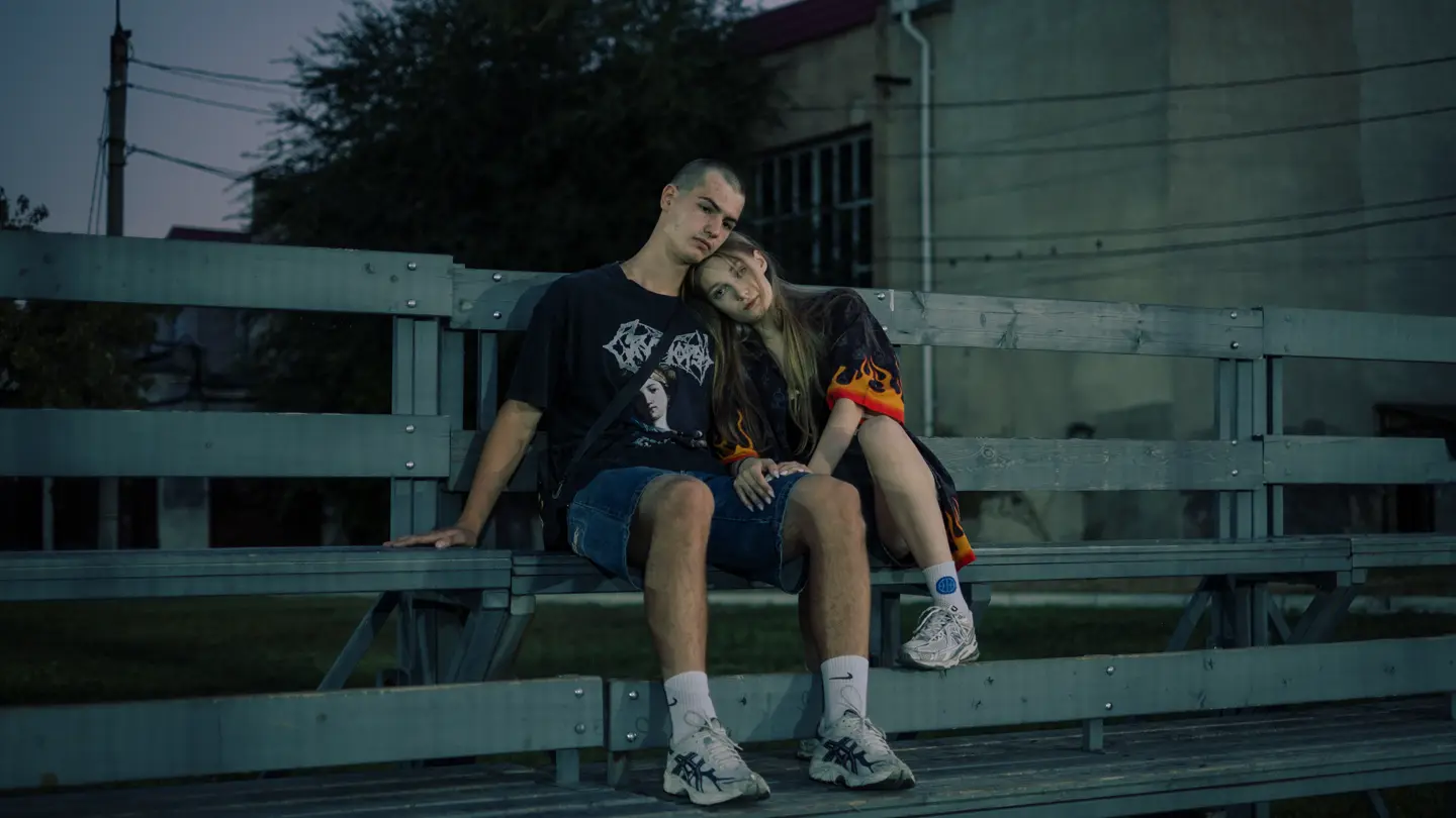 A teenage couple is sitting on a bench, and her head is resting on his shoulder.