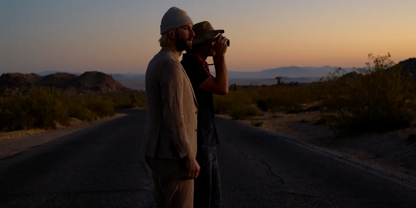 Garrett and Gantry Hill in a desert landscape at sunset, one looking through a camera.