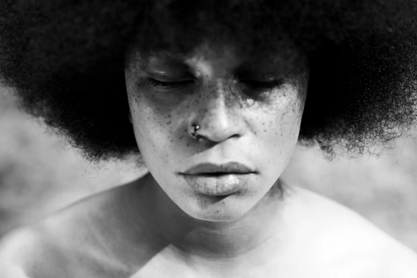 A close-up of a person with closed eyes and Afro hairstyle in black and white