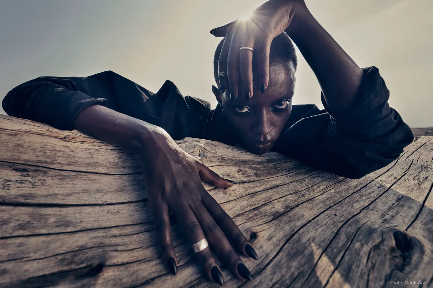A young woman is peeking out from behind a tree trunk