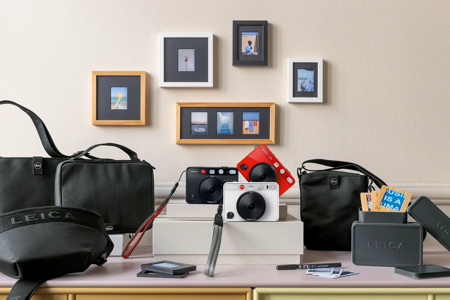 Leica cameras and accessories on a table, with framed photos on the wall in the background.