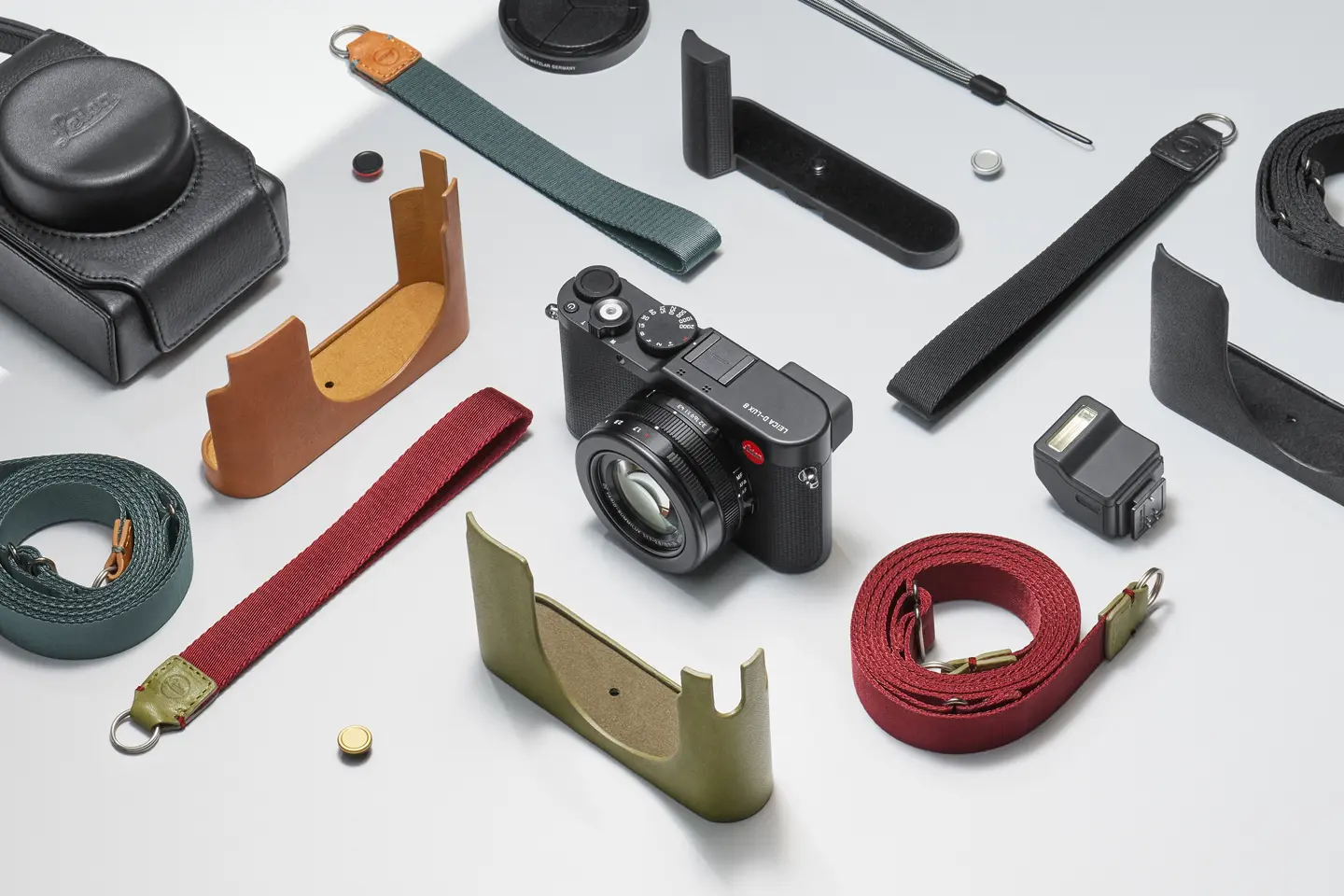 Leica camera with various straps, protective covers and accessories on a light background.