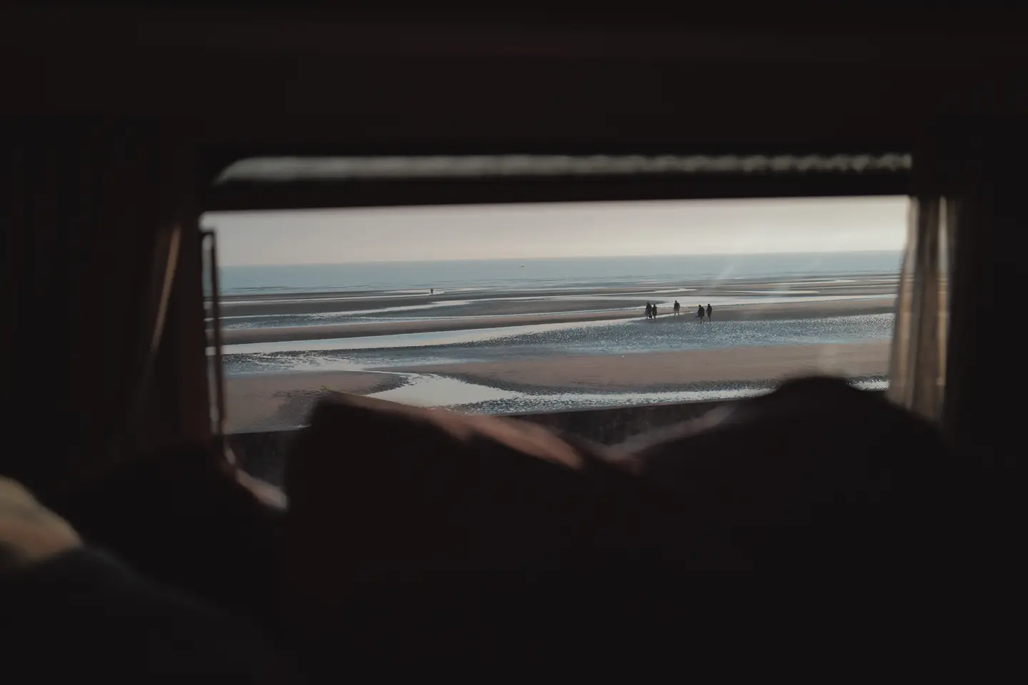 People on the beach photographed from a small window of a caravan