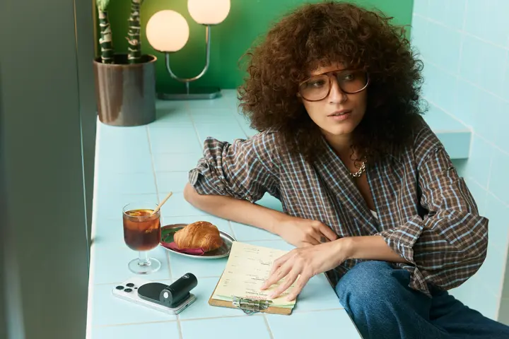 Woman sitting at a counter with a Leica LUX Grip, a croissant and a drink