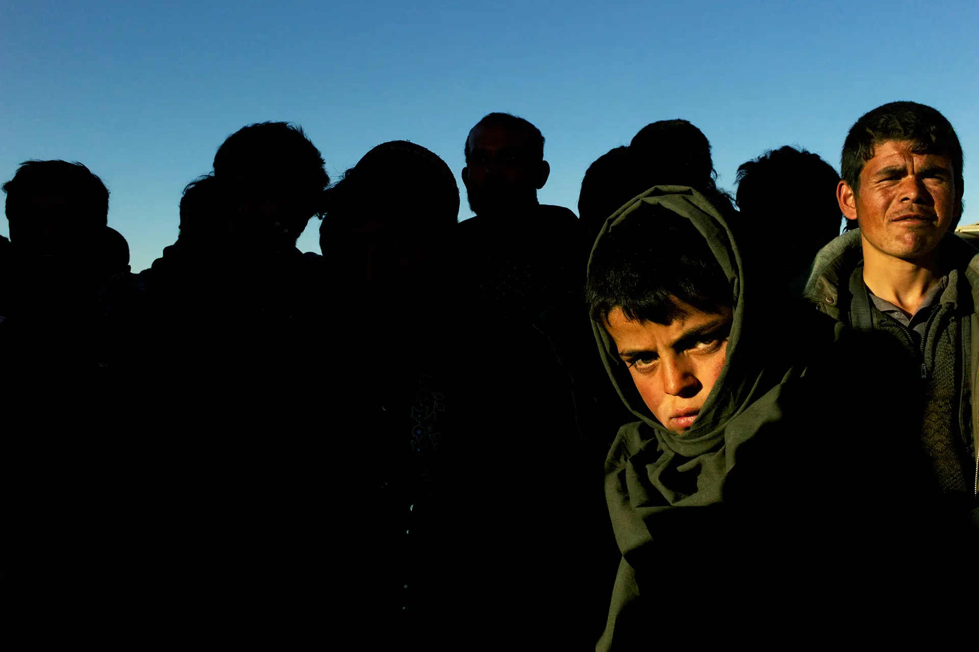 Two people standing in the sun in front of a group of people in the shade