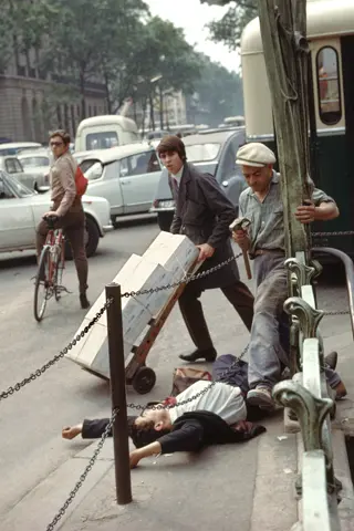 A young man in a suit and tie lies on his back with arms stretched above his head, directly next to the metro station